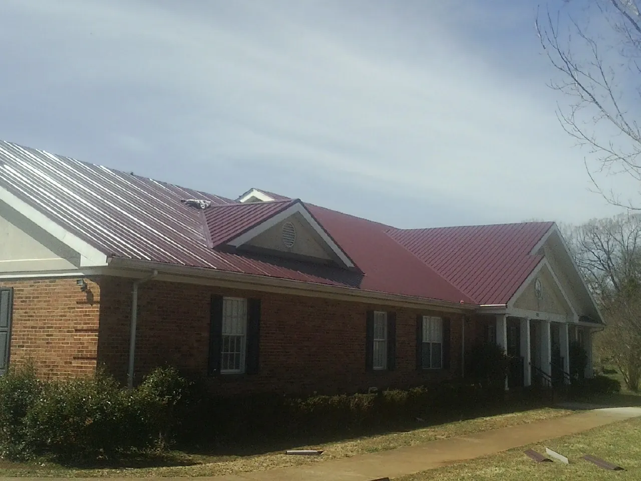 Red metal roof with gabled entries on a long brick building, from a Hail Damage Roof Repair job in Great Barrington