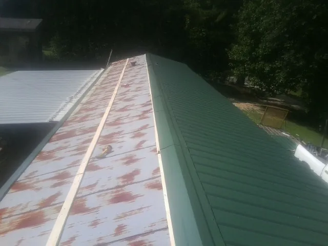 Old rusted panels beside newly installed green metal roofing — Wind Damage Roof Repair by Roofing Brothers in Great Barrington