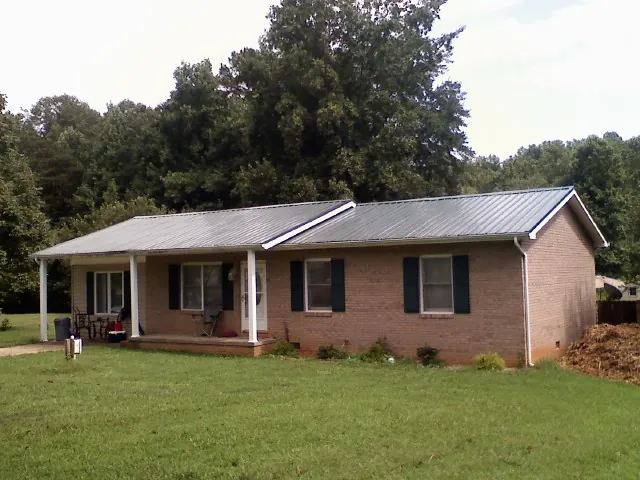 Gray metal roof on a brick ranch house with a side carport in Great Barrington