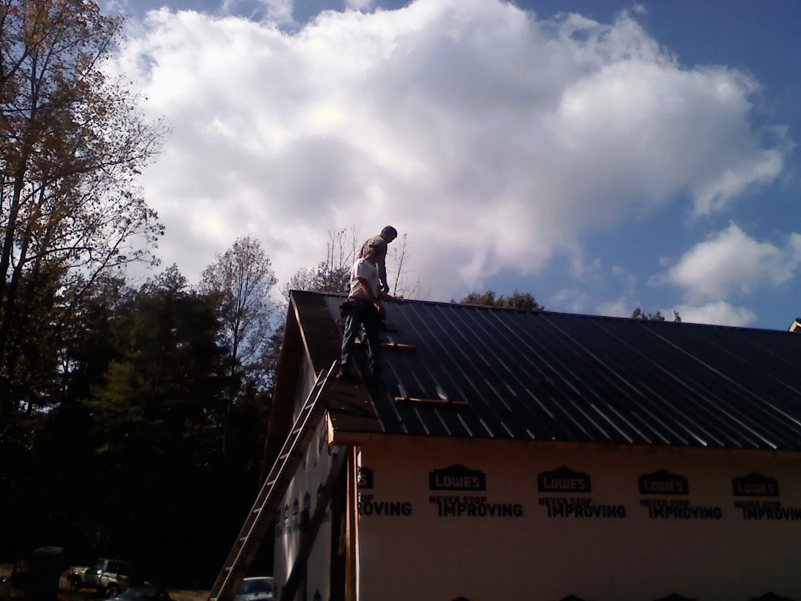 Roofer fastening dark metal panels high against a cloudy sky, from a Roof Inspection job in Great Barrington