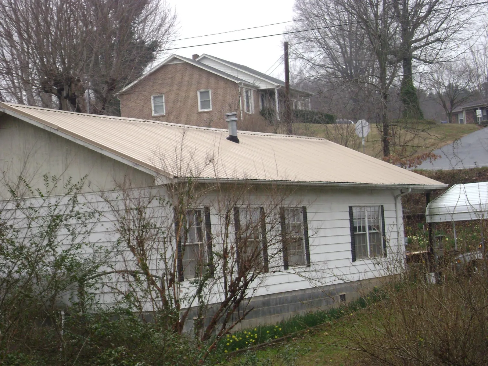 Tan metal roof on a white sided house set into a hillside — Commercial Roofing by Roofing Brothers in Great Barrington