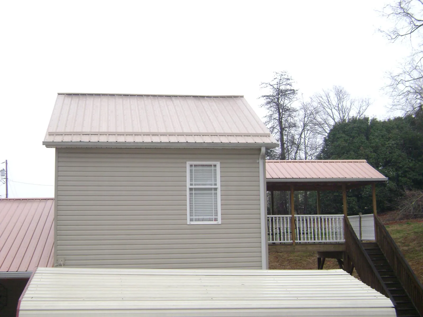 Tan metal roofs on a two story addition and attached porch, from a Roof Replacement job in Great Barrington