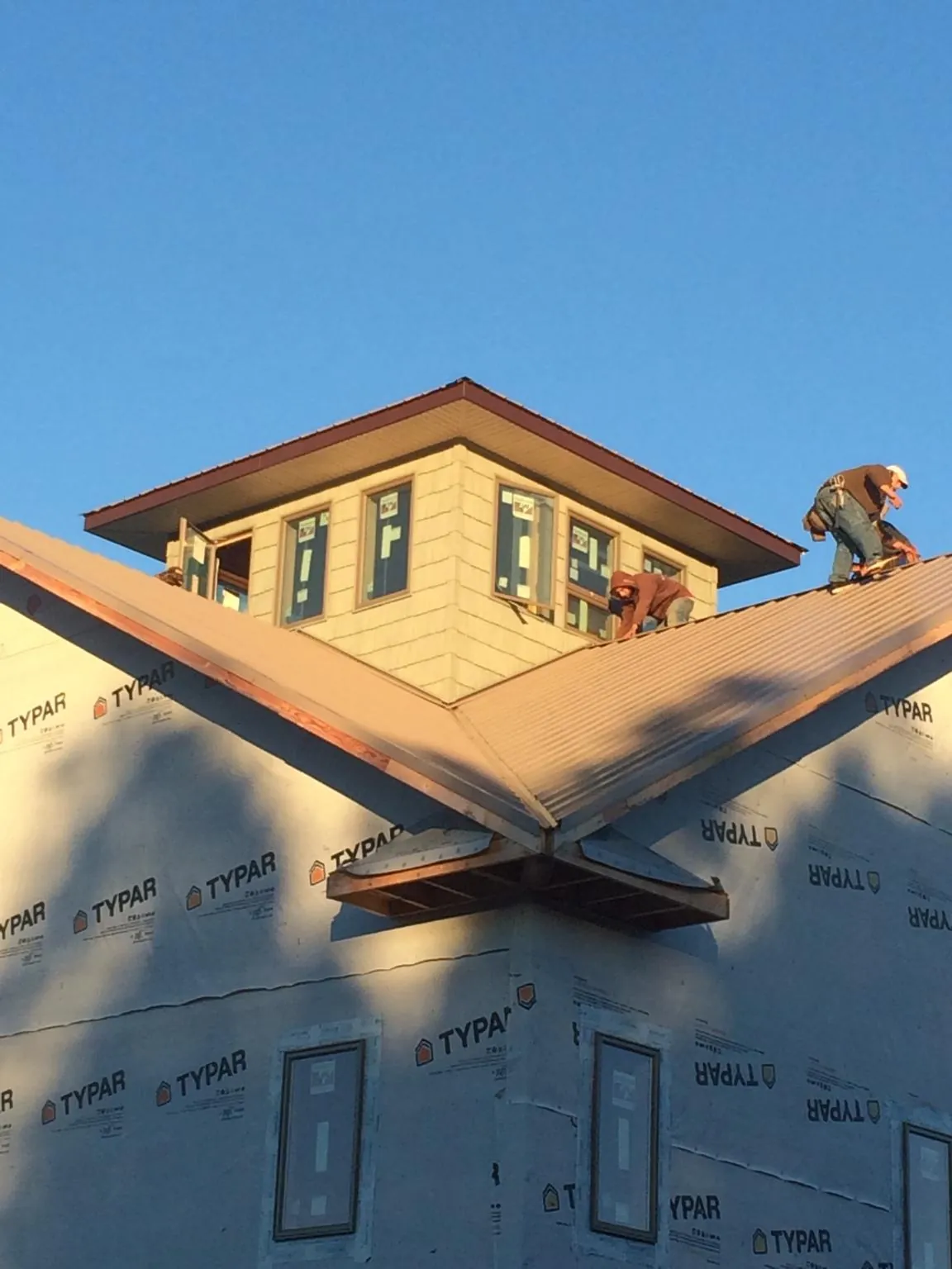 Roofers working around a rooftop cupola on a new metal roof at sunset — Roof Waterproofing in Great Barrington by Roofing Brothers